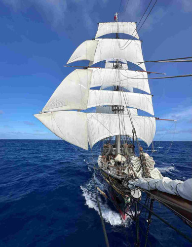 View of a Tallship from the very front with five square sails on the fore mast and three stun sails on the starboard yards.  All the fore stay sails are stowed. 