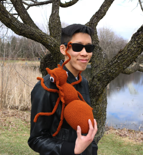 A very cool dude with shades smiles holding a massive amigurumi stuffed ant. He even has on a leather jacket. 

makes you want to give up trying to be cool ...who could beat him??

The ant is brown and fairly realistic about a foot long. 