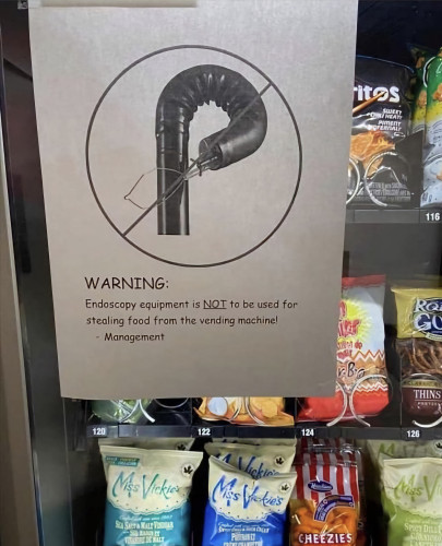 A vending machine with a sign taped on the front. It reads: Warning: endoscopy equipment is not to be used for stealing food from the vending machine. Management. Then there's a picture of a long, tubular endoscope 