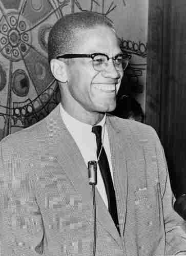 Malcolm X in March 1964, in a suit and tie, and his characteristic horn-rimmed glasses, smiling. By Ed Ford, World Telegram staff photographer - Library of Congress. New York World-Telegram &amp; Sun Collection. http://hdl.loc.gov/loc.pnp/cph.3c15058, Public Domain, https://commons.wikimedia.org/w/index.php?curid=3515550