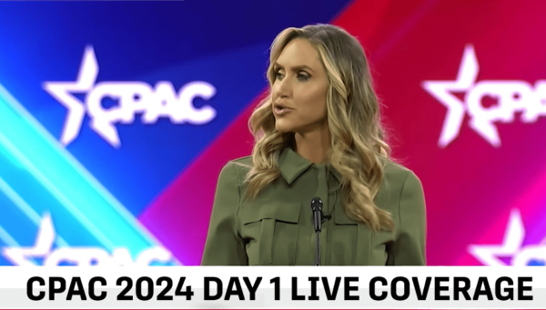 A woman at CPAC speaking. She has on TV makeup, fake eyelashes, blonde highlighted hair, and silk khaki blouse styled like a military shirt. 

Her name is Laura Trump.