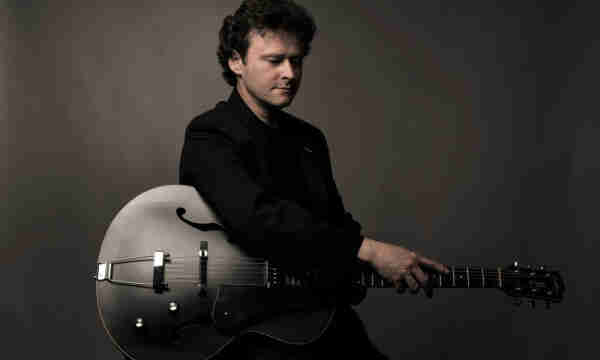 A photo of Jazz guitar player Sylvain Luc, holding one of his guitar.