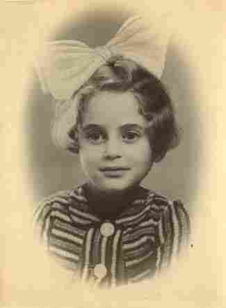 A portrait photo of the face of a young girl. SHe has wavy hair covering her ears and a huge bow on her head. She is wearing a striped blouse with large buttons.