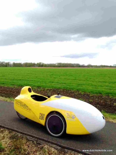 Velomobile on the way to a customer in the countryside. The light coloured stripe in the background is a field of tulips.