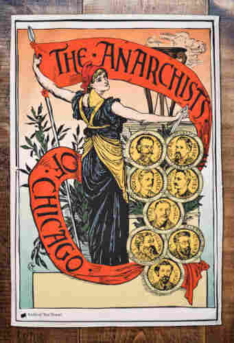 Woman holding a long red banner that reads "The Anarchists of Chicago," with small, medallion busts of the 8 men convicted of the Haymarket bombing.
