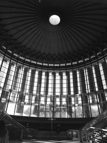 My photo using a black and white filter of the entrance with a circular roof and row of windows and pillars with an escalator on each side