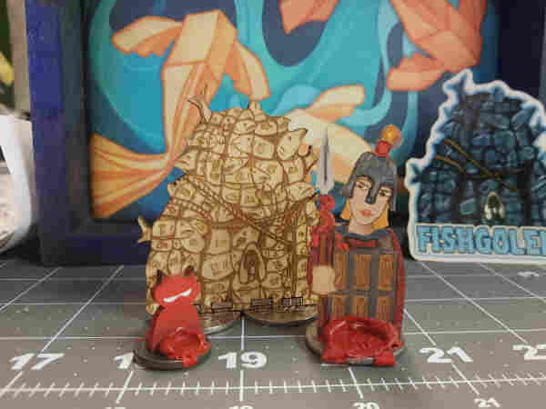 Photo of 3 lasercut minis, all on coin bases, the largest is an unpainted fishgolem.