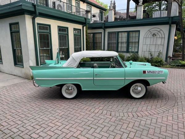This 1967 Amphicar Model 770 was purchased by the current owner from the original owner in 1987. It is finished in Fjord Green over white and green vinyl and powered by a 1,147cc Triumph inline-four paired with a two-part manual transmission delivering four forward speeds and reverse on land along with forward and reverse on water. Features include a white convertible top, a top boot, 13″ steel wheels, whitewall tires, navigation lights, a marine horn, two bilge pumps, rear tail fins, and bumper/propeller guards.