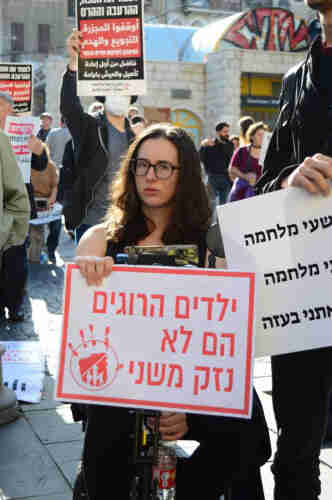 A person holding a sign that reads “Dead Children Are Not Collateral Damage” in Hebrew.