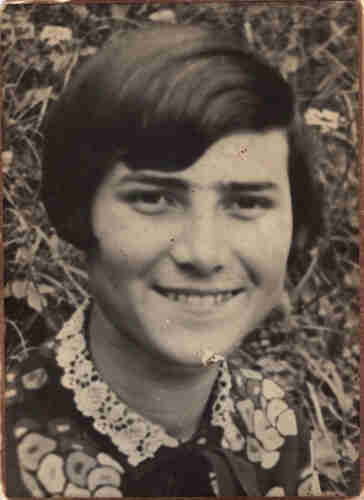 A portrait photo of a face of a young women photograhed in the background of some grass. She is smiling and has a blouse with floral patterns.