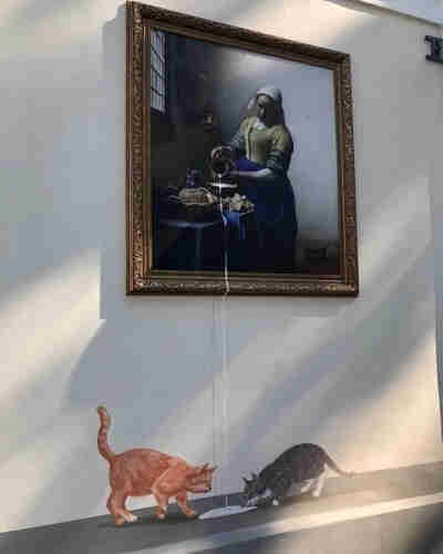 A painting of a woman pouring milk, and it spills out of the painting and onto the floor below, where two cats lick it up.