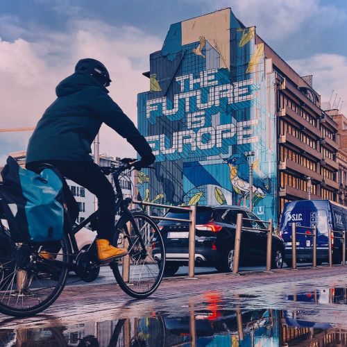 Cyclist pedalling in a bike lane in front of The Future is Europe mural.  © European Union, pic by Julia Celis 2023
