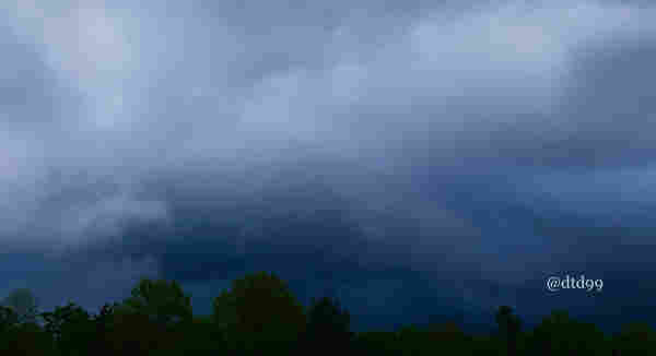 Dark storm clouds over a tree line with a watermark in the bottom right corner.
