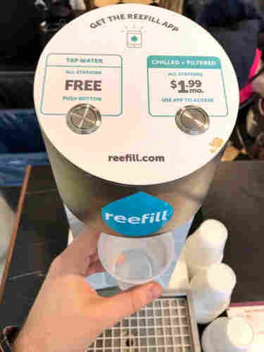 A photo of a 'reefill' water dispenser. There are two buttons. One says 'Tap water, FREE, push button' the other says 'Chilled and filtered, all stations, $1.99 per month, use app to access'.