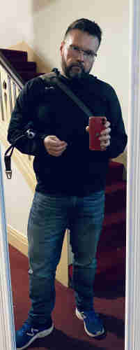 Angry-ass homo, new balance dad(dy) shoes, jeans, new balance dad(dy) windbreaker, over the shoulder bag, umbrella under the arm, scowl, foyer mirror selfie. 