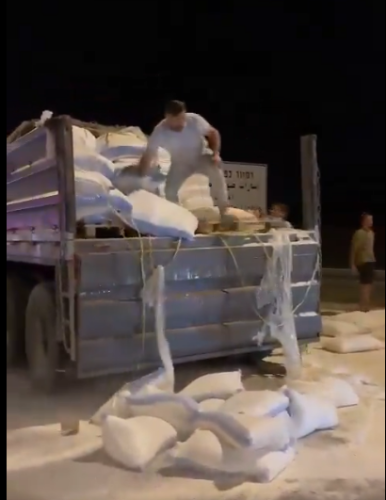 An Israeli throwing opened sacks of aid to the floor from the back of an aid delivery truck.