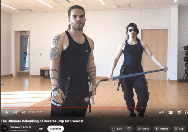 still from a video titled "the ultimate debunking of reverse grip for swords" by "sellsword arts"

a guy in a black tank top that shows off his tattooed muscle arms is talking to the camera. slightly behind him is his friend, similarly attired but wearing black sunglasses and one of those little "you broke your nose" strips, casually holding a practice longsword