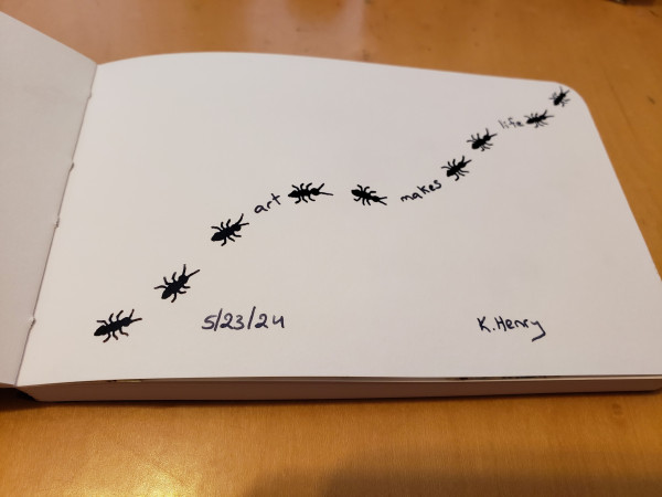 Hand drawn generative art in ink on an open page of my sketchbook. The abstract pattern has a repeating ant motif, as if they are crawling along a curvy line. Between the ants there is some text that says "art makes life"
