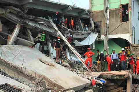 Side view of the collapsed building, with rescue workers in masks and orange jumpsuits. By Sharat Chowdhury - Sharat Chowdhury&#039;s facebook album, permission given by email: https://www.facebook.com/media/set/?set=a.10151367557176814.1073741835.723176813, CC BY 2.5, https://commons.wikimedia.org/w/index.php?curid=25784003