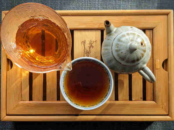 A teapot, glass pitcher, and porcelain cup filled with drunken begonia yancha (rock tea) on a bamboo tray. 