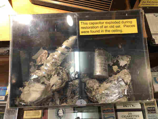 A big mess of metal with a yellow sign that reads ‘This capacitor exploded during restoration of an old set. Pieces were found in the ceiling.’
