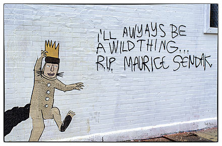 Graffiti on a white brick wall, with an image of Max, from the book, "Where the Wild Things Are," in a yellow crown. Reads: I'll always be a wild think...R.I.P. Maurice Sendak.