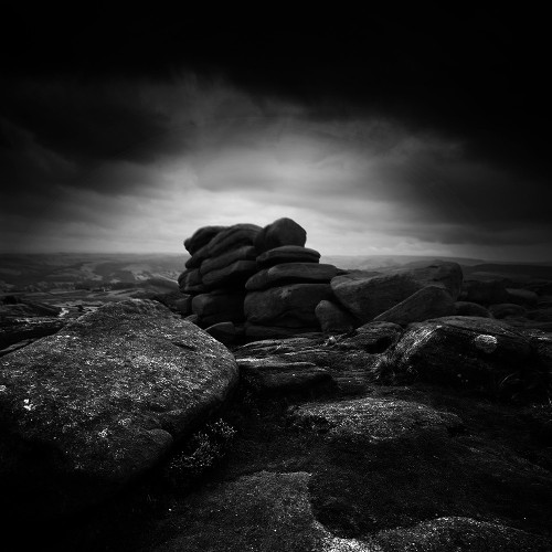 Atmospheric black and white photo of a rocky outcrop under a dark sky.