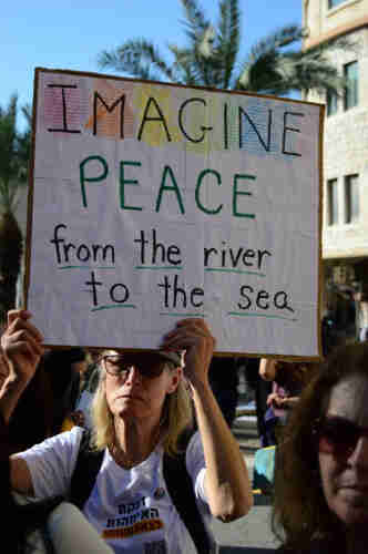 A woman holding a sign above her head that reads: “IMAGINE PEACE from the river to the sea”.
