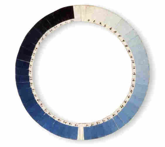 A circular wooden contraption with squares of color painted  along the edge in a ring. The colors move from the whitest white through every shade of blue and into blacks at the end 