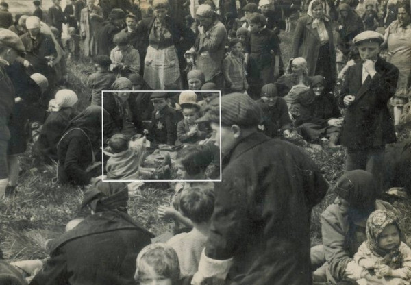 Black and white historical photo showing a large crowd gathered in an outdoor setting, with several individuals seated and interacting near the center. Hungarian Jews at Auschwitz II-Birkenau waiting to be murdered in a gas chamber.