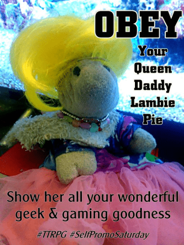 Lamb Beanie Baby sitting on a red hardcover book in from of a television with an aquarium on the screen. She is wearing a bright yellow wig, multiple charm necklaces, a fake fur stole or hood, and a fancy doll dress with a blue purple and white top and a big multi-layer frilly pink bottom. 

Top text: OBEY Your Queen Daddy Lambie Pie
Bottom text: Show her all your wonderful geek & gaming goodness #TTRPG #SelfPromoSaturday