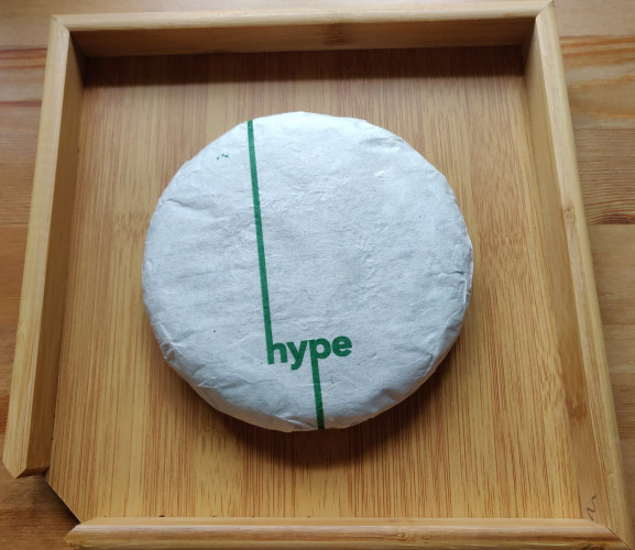 A full wrapped tea cake on a bamboo tea tray. The tea is 2024 Green Hype from White2tea