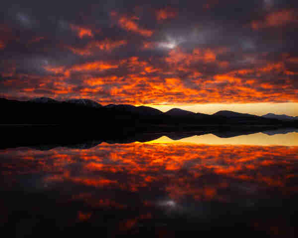 Atardecer sobre el lago Garry, Escocia, reflejando perfectamente el cielo completamente cubierto de nubes y su espectacular tono naranja.