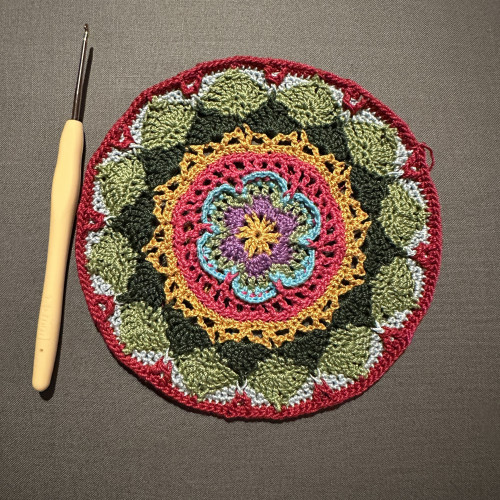 A small crocheted mandala. There is a 1.5mm crochet hook next to it. 