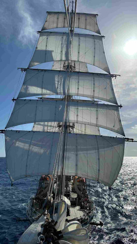 Square rigged ship viewed from jib boom with shadows of main mast on the fore sails. 