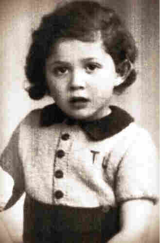A photo of a young boy in a blouse with large buttons and short sleeves. He has quite long hair and open mouth.