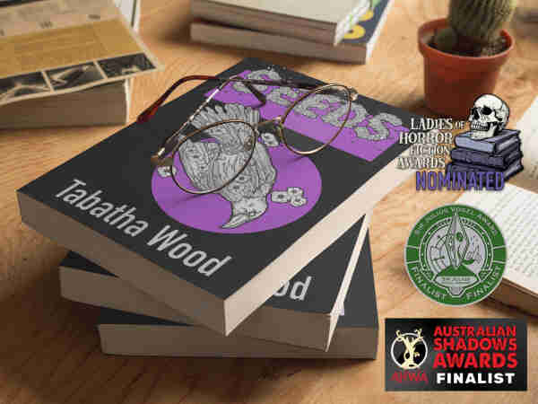 A stack of books with the title SEEDS by Tabatha Wood. A pair of glasses is on the top and there are some graphics showing that the book was nominated for awards: Ladies of Horror Fiction, SJV Award and Australasian Horror Writers Association