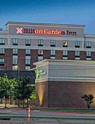 A brick hotel with the sign "Hilton Garden Inn". Some of the letters have burned out, so only "on Garde" can be seen