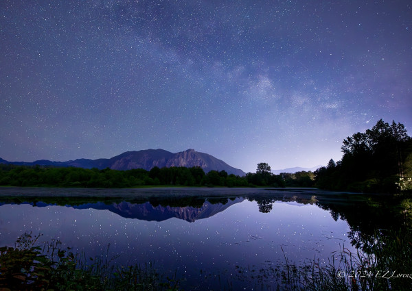 Nightsky over Mount Si with the mountain and stars reflected in a pond. The Milky Way is faintly visible. Single shot. 