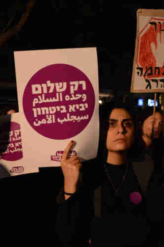 A woman holding a sign next to her head that reads: “Only Peace Will Bring Security” in Hebrew and Arabic.