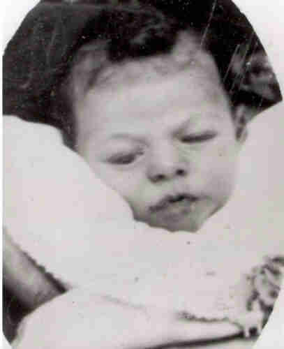 A blured headshot photograph of a baby boy. You can only see his head surrounded with some white blanket. He has dark hair. 
