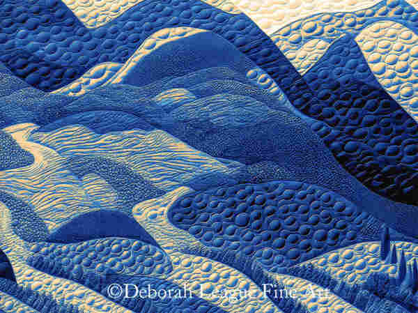 A complex pattern of blue and gold textured forms creates an abstract mountain landscape. The raised, bubble-like shapes and rippled lines suggest a tactile, three-dimensional, quilted quality.