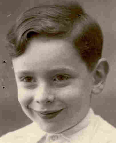 Picture of the face of a young boy in a white shirt buttoned up to the neck. He is smiling. He has short hair and a fringe pulled to the right side - slightly wavy.