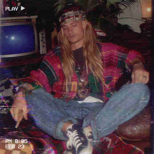 An individual who appears to be in a state of deep relaxation or asleep, evoking a sense of being heavily under the influence, possibly due to the blunt that they are holding. They are slouched on a leather couch, sporting a 90s-inspired outfit with a colorful patterned jacket and a bandana headband, eyes closed and mouth open slightly, which suggests that they have dozed off. Their loose jeans and sneakers add to the laid-back vibe. The setting includes a retro television in the background, contributing to the vintage atmosphere. The visual is overlaid with a VHS-style filter, displaying the play icon in the corner and a timestamp at the bottom indicating “PM 8:05 FEB 23,” reinforcing the concept that this snapshot captures a moment of intense relaxation or intoxication.