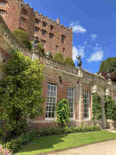 Historic Powis Castle a beautiful red brick building with ornate windows, sculptures, and well-manicured garden under a blue sky with scattered clouds.