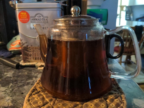 Glass teapot filled with tea. Large Ahmad Tea tin of Earl Grey in the background.