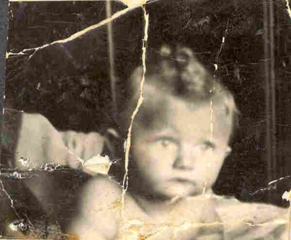 A baby boy lying on some blanket. Just the head and some shoulders are visible. A large lock of blond hair at the top of the head. The boy is looking with wide-open eyes in front of him - to the right side of the frame.