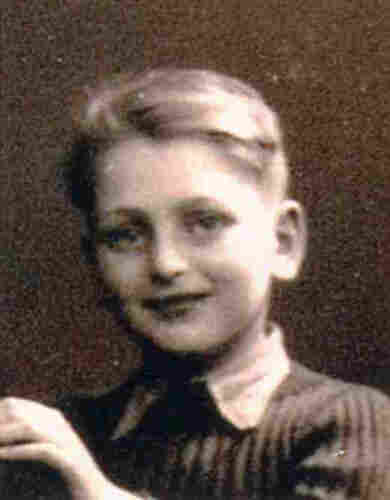 Portrait photograph of a young boy wearing a dark striped jumper with a protruding collar. He has short, side-swept hair. He is smiling slightly, looking into the camera with large eyes.