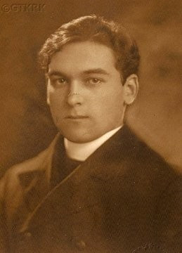 Vintage sepia-toned portrait of a man with short hair, wearing a dark jacket and white shirt, looking directly at the camera. A catholic priest.
