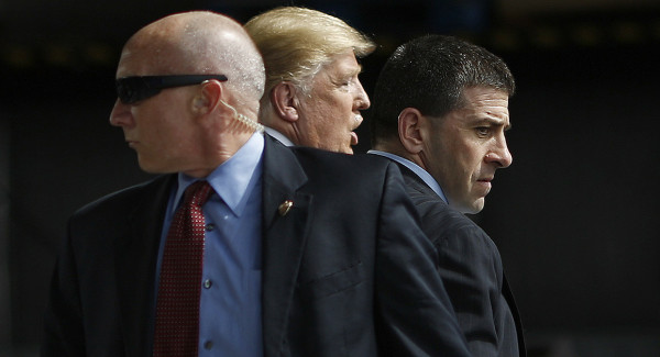 President Donald Trump, closely flanked by two Secret Service agents, alert: one closely watching Trump’s front, the other closely watching the area behind him.